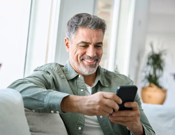Hombre sentado en el sofá mientras utiliza su teléfono móvil