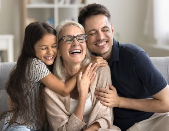 Familia de abuela, padre e hija abrazándose felices mientras están sentados en el sofá