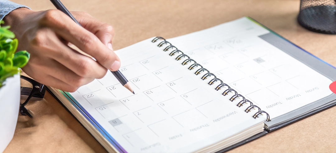 Mano derecha sosteniendo un lápiz y anotando en una agenda abierta