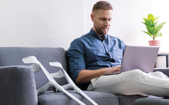 Persona con muletas utilizando un ordenador portátil en el salón